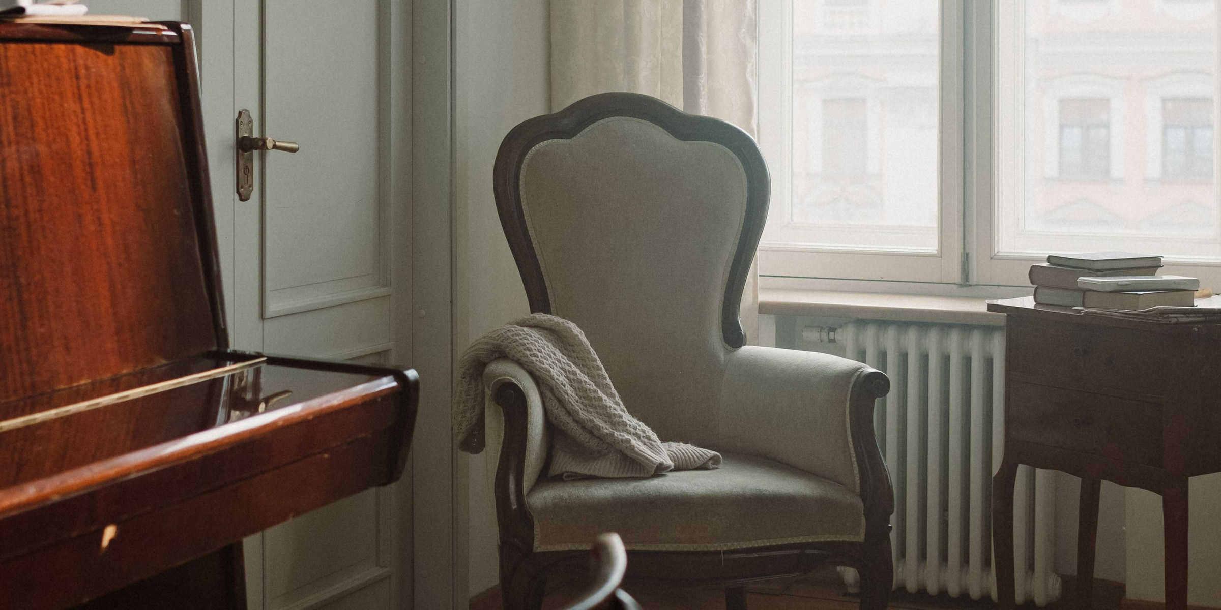 Altbauzimmer mit Klavier, Sessel und hohem Fenster