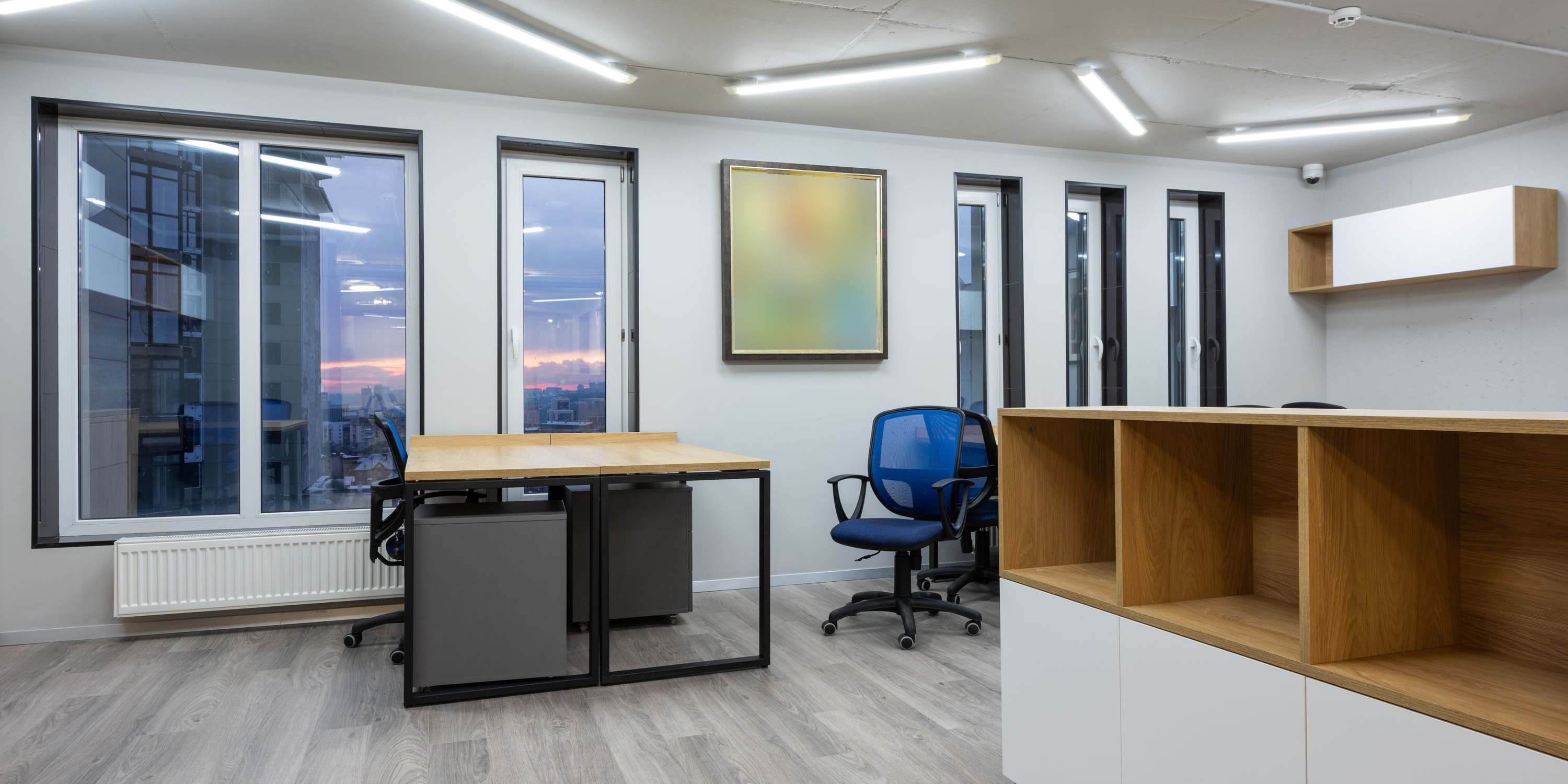 Modernes, aufgeräumtes Büro mit Schreibtisch, Rollcontainern und Bürostuhl vor einer Fensterfront