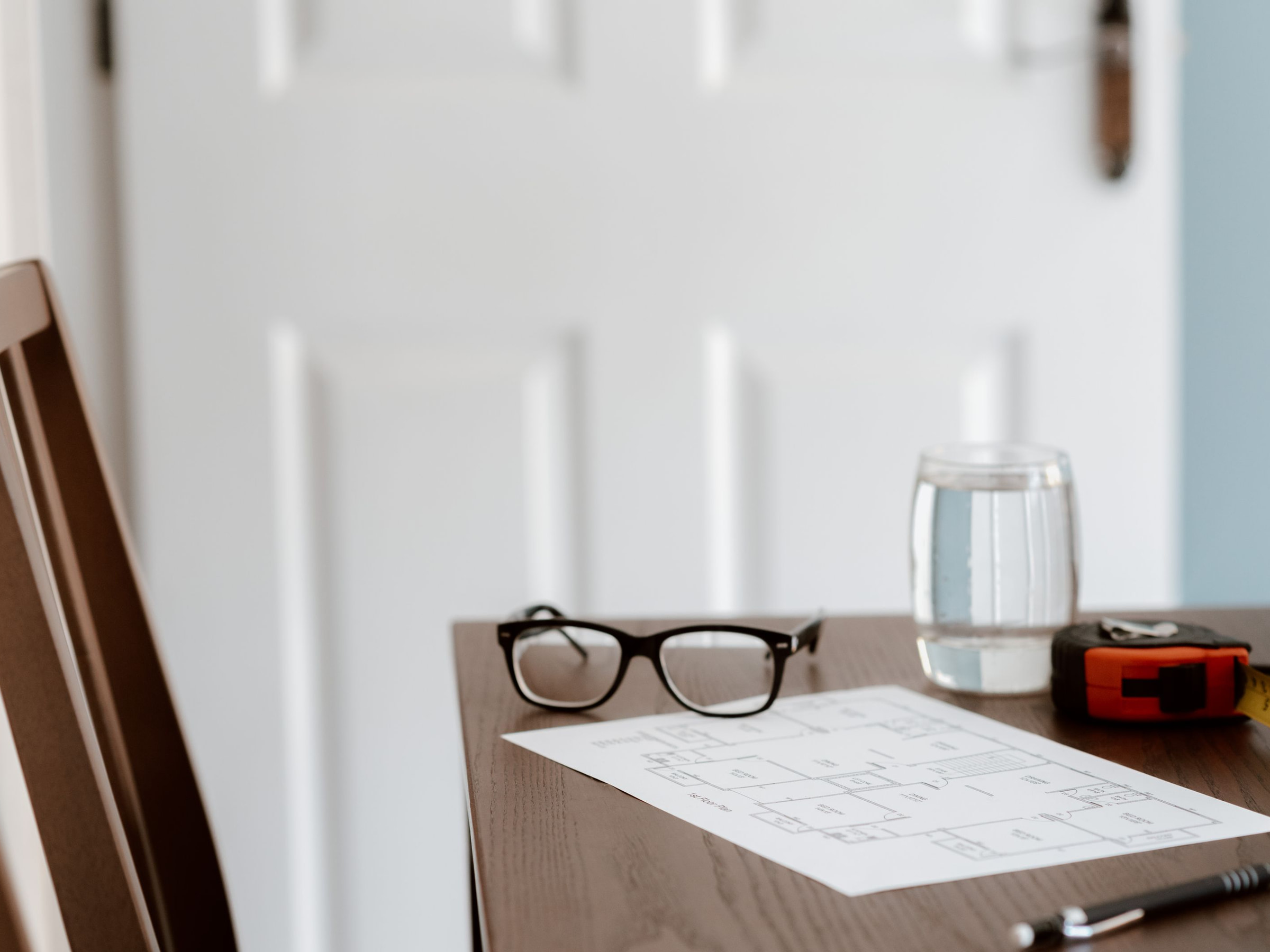 Schreibtisch mit Brille, einem Grundriss, einem Wasserglas und einem Maßband