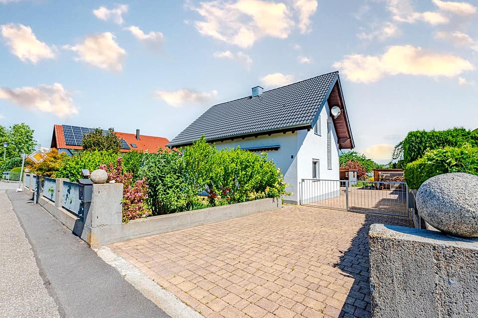 Weiß verputztes Einfamilienhaus in Mariaposching mit dunklem Satteldach, gepflasterter Zufahrt und bepflanztem Vorgarten
