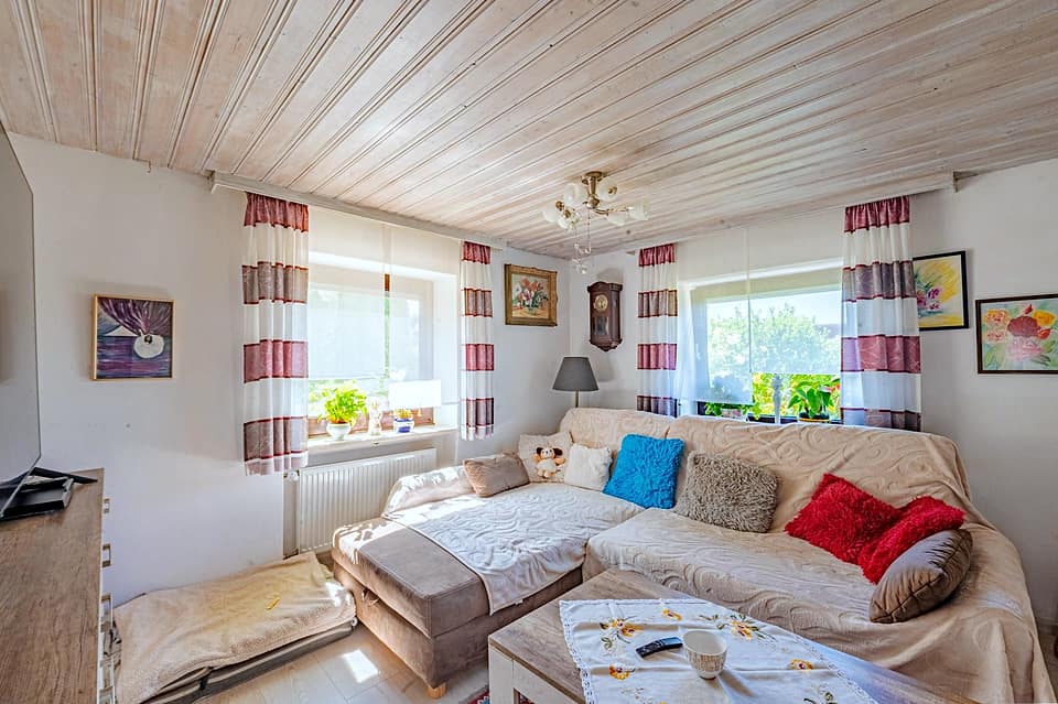 Wohnzimmer mit heller Polstergarnitur, Holzdecke und Fenstern zum Garten