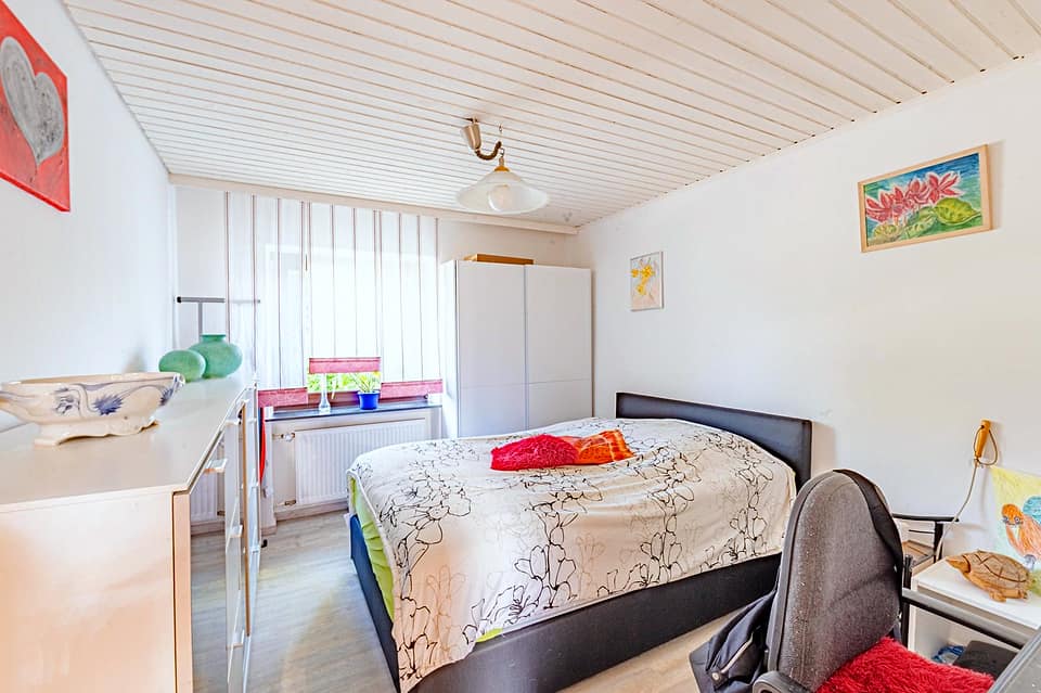Helles Schlafzimmer unter der Dachschräge mit Bett und Arbeitsplatz am Fenster