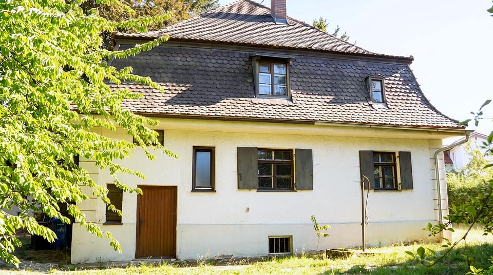 Seitenansicht mit Holztür, Kellerfenstern und Wiese ringsum