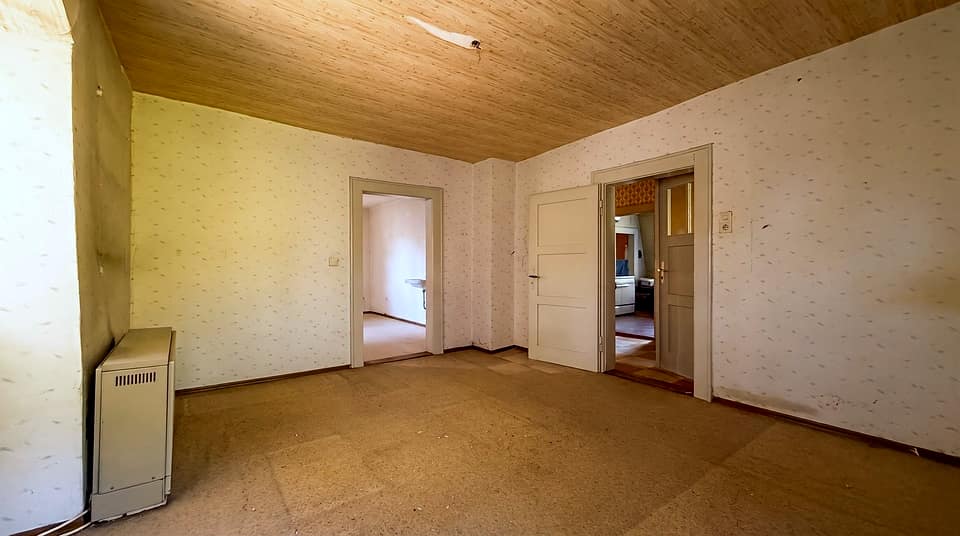 Leerer Wohnraum mit Holzdecke, Tapete und zwei Türen