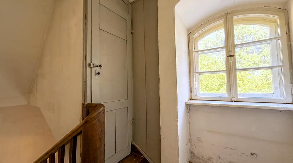 Treppenpodest mit Holzgeländer und hohem Sprossenfenster