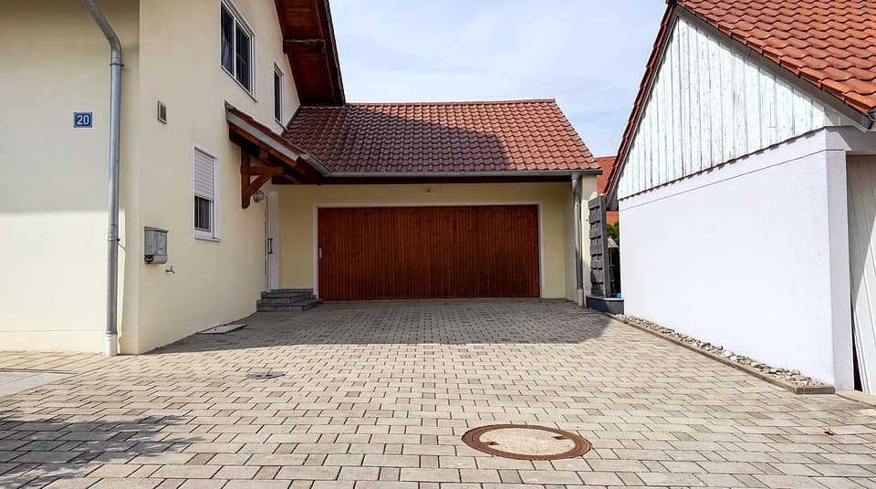 Gepflasterte Zufahrt zur Doppelgarage zwischen Haus und Nebengebäude