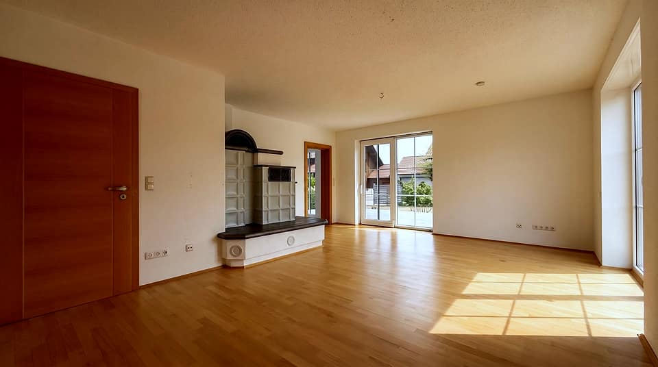Leeres Wohnzimmer mit Kaminofen, Parkett und bodentiefem Fenster