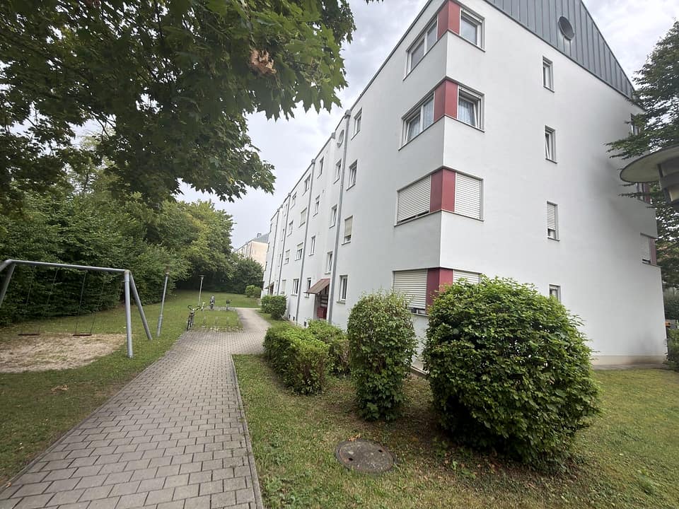 Gepflasterter Weg an der Rückseite des Wohnblocks mit Rasen und Spielfläche