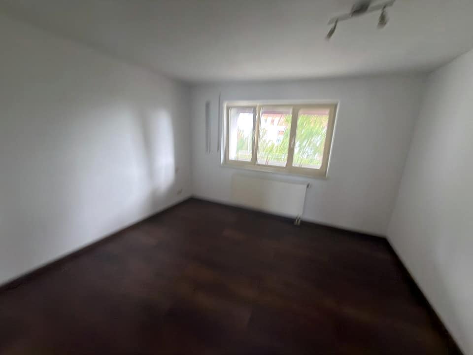 Drittes Zimmer mit dunklem Boden und Fenster zur Grünanlage