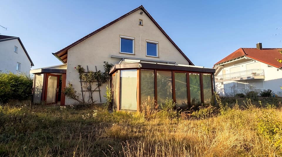 Haus mit gläsernem Wintergarten, davor die Wiese des Grundstücks