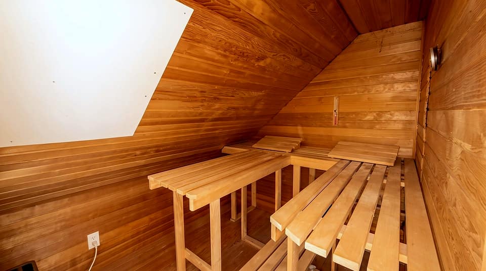Sauna aus hellem Holz mit zwei Liegebänken unter der Dachschräge