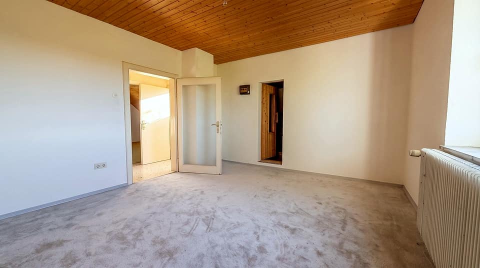 Zimmer mit Holzdecke, hellem Boden und zwei Türen