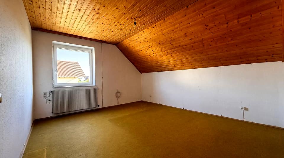 Dachzimmer mit Holzschräge, Fenster und grünem Bodenbelag