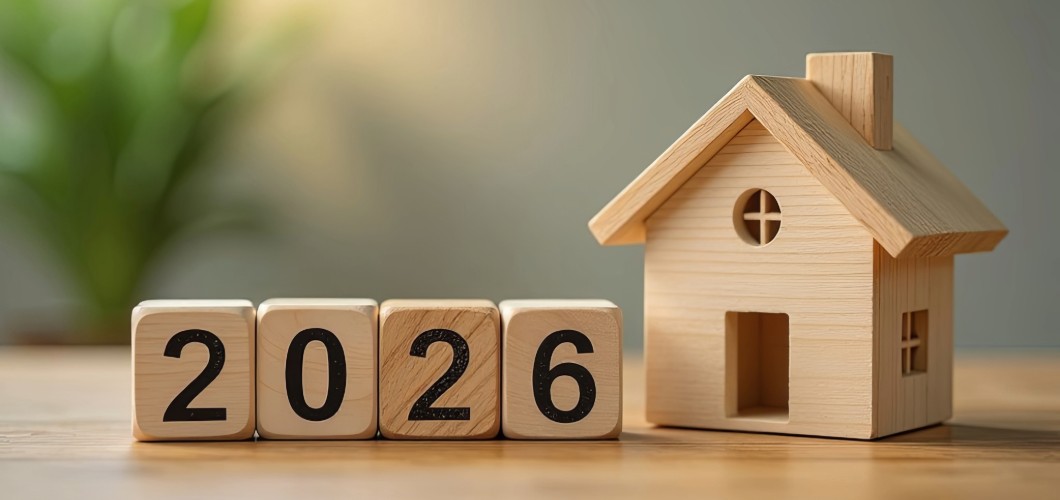 Ein Hausmodell aus Holz neben Würfeln, die das Jahr 2026 zeigen